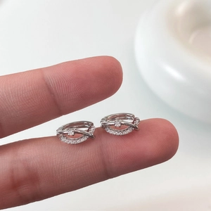 Détail de boucles d'oreilles créoles croisées en argent serties de zircons pavés