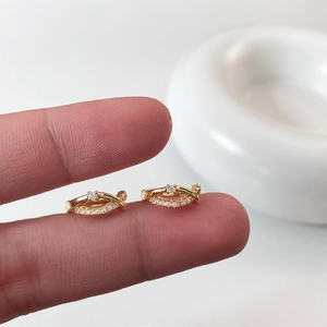 Détail de boucles d'oreilles croisées plaquées or avec zircons cubiques sur les doigts