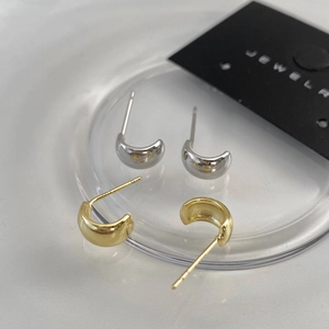Close-up of minimalist C-shaped polished gold and silver bean stud earrings on a display tray