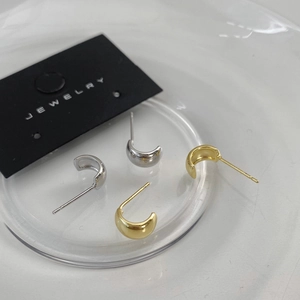 Macro view of C-shaped half-round stud earrings in polished gold and silver finishes