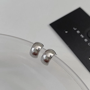 Macro shot of minimalist silver polished semi-hoop earrings on transparent glass