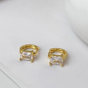 Macro detail of gold-plated hoop earrings with sparkling emerald-cut square zirconias