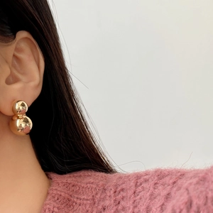 Polished gold double ball stud earrings in minimalist gourd shape worn by a model