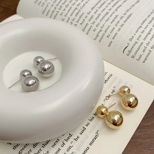 Detailed close-up of gold and silver double ball stud earrings on a ceramic tray