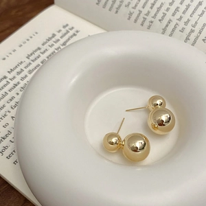 Detail of polished gold double ball earrings on a white ceramic tray with vintage book page