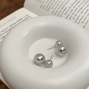 Close-up of polished silver metal double ball stud earrings on a white ceramic tray