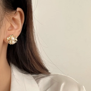 Élégantes boucles d'oreilles fleurs plissées dorées avec perles blanches portées par un mannequin