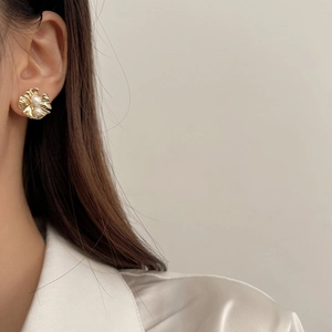 Boucles d'oreilles fleur plissée dorée avec deux perles blanches portées par un mannequin