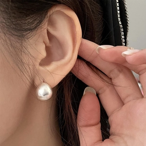 Close-up of minimalist polished silver drop earrings worn on a model's ear