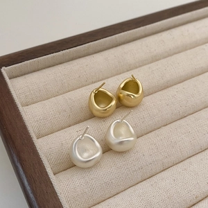 Macro detail of gold and silver matte waterdrop stud earrings on a velvet jewelry tray