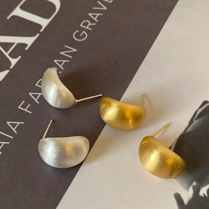 Detail of brushed gold and silver crescent stud earrings on a minimalist backdrop