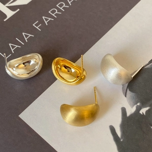 Detailed view of curved bean stud earrings in polished gold and matte silver finishes