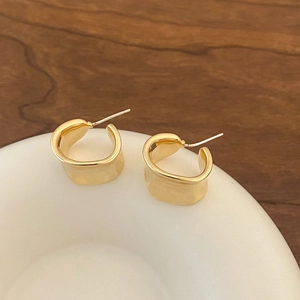 Detailed view of wide irregular geometric C-shaped gold-plated hoop earrings on a ceramic dish