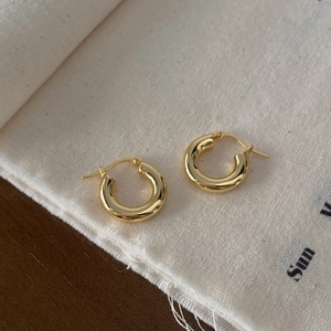 Vue détaillée de boucles d'oreilles créoles dorées polies sur fond en tissu minimaliste