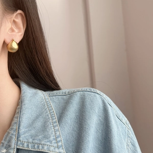 Orecchini a goccia in oro opaco con finitura spazzolata indossati da una modella per uno stile