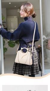 Detail of a beige handbag with unique cat-ear metal handles and gold trim accent