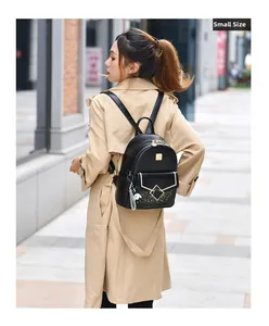 Detail of a small black leather backpack with gold metal logo and dog charm on a model