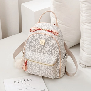 Mini beige monogram backpack with red bow and faux fur pompom in a minimalist setting