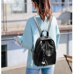 Close-up of black faux leather backpack with multiple zippers and cute bear keychain