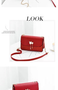 Detail of red leather crossbody bag with golden cat-shaped pearl tassel buckle and chain
