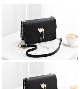 Detail of black leather chain bag featuring a pearl cat ornament and flap closure