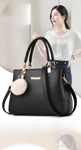 Detail of matte black leather handbag featuring gold hardware and a fluffy beige charm