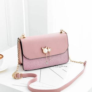 Pink sequin crossbody bag with pearl cat metal ornament and golden chain strap on white desk
