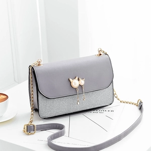 Grey patchwork crossbody bag with pearl cat pendant and gold chain strap on table