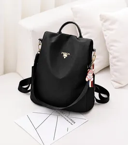 Detalle de mochila negra impermeable de tela oxford con colgante de oso en sofá blanco