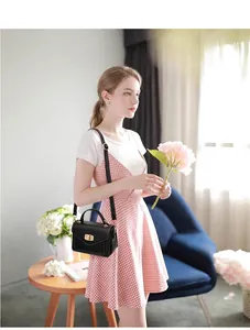 Retro schwarze Umhängetasche mit goldenem Drehverschluss, von einem Model lässig getragen