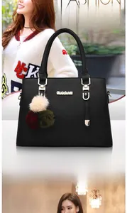 Detail of black litchi pattern handbag with gold hardware and tricolor pompom charm