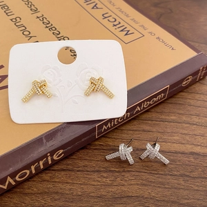 Knoten-Ohrstecker mit funkelnden Zirkonia in Gold und Silber auf einem Buch-Hintergrund