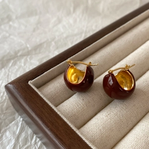 Detail view of burgundy enamel bean earrings with gold plating in a luxury jewelry box