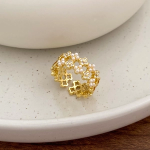 Macro shot of gold floral ring featuring pearl and zircon inlay on a ceramic bowl