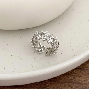 Detailed view of silver open ring featuring intricate hollow flower patterns and pearls