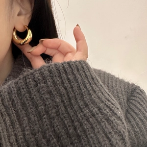 Close-up of thick gold-plated hoop earrings on a model wearing a grey sweater