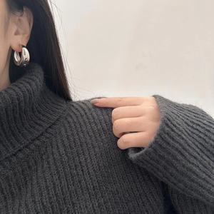 Close-up of polished silver thick hoop earrings worn with a minimalist grey sweater
