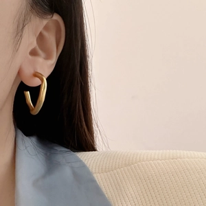 Close-up of matte gold irregular C-shape hoop earrings on a model with minimalist style