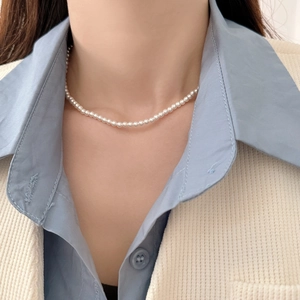 Elegant white round pearl choker necklace worn with a light blue shirt and tweed jacket