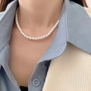 Close-up of elegant single-layer white round pearl necklace worn with a knitted vest