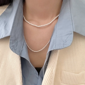Close-up of double-layer necklace set with small white pearls and a thin sparkling metal chain