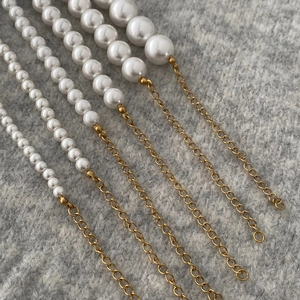 Detail view of round pearl necklaces in various sizes with golden metal extension chains
