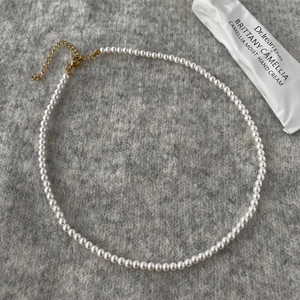 Close-up of elegant round white pearl necklace with gold lobster clasp on grey knit