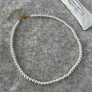Detail of round shell pearl necklace with golden lobster clasp on grey knit background
