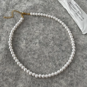 Detailed close-up of high-quality round white pearl necklace on grey felt with gold clasp