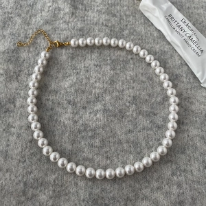Detailed shot of round white pearl necklace with adjustable gold clasp on grey knit fabric