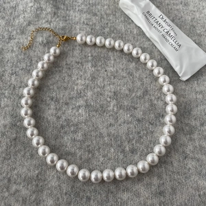 Detail view of round white pearl necklace with golden lobster clasp on textured fabric
