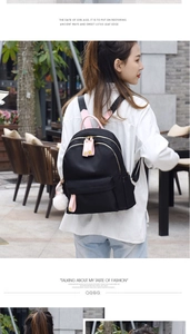 Detail of black oxford nylon backpack with pink straps and a white fluffy pompom charm
