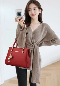 Détail du sac à main rouge en cuir grainé avec poignée dorée et pendentif floral