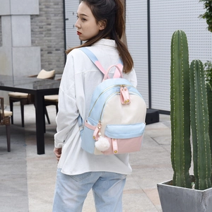 Chic tricolor patchwork nylon backpack with pompom charm on female model outdoors